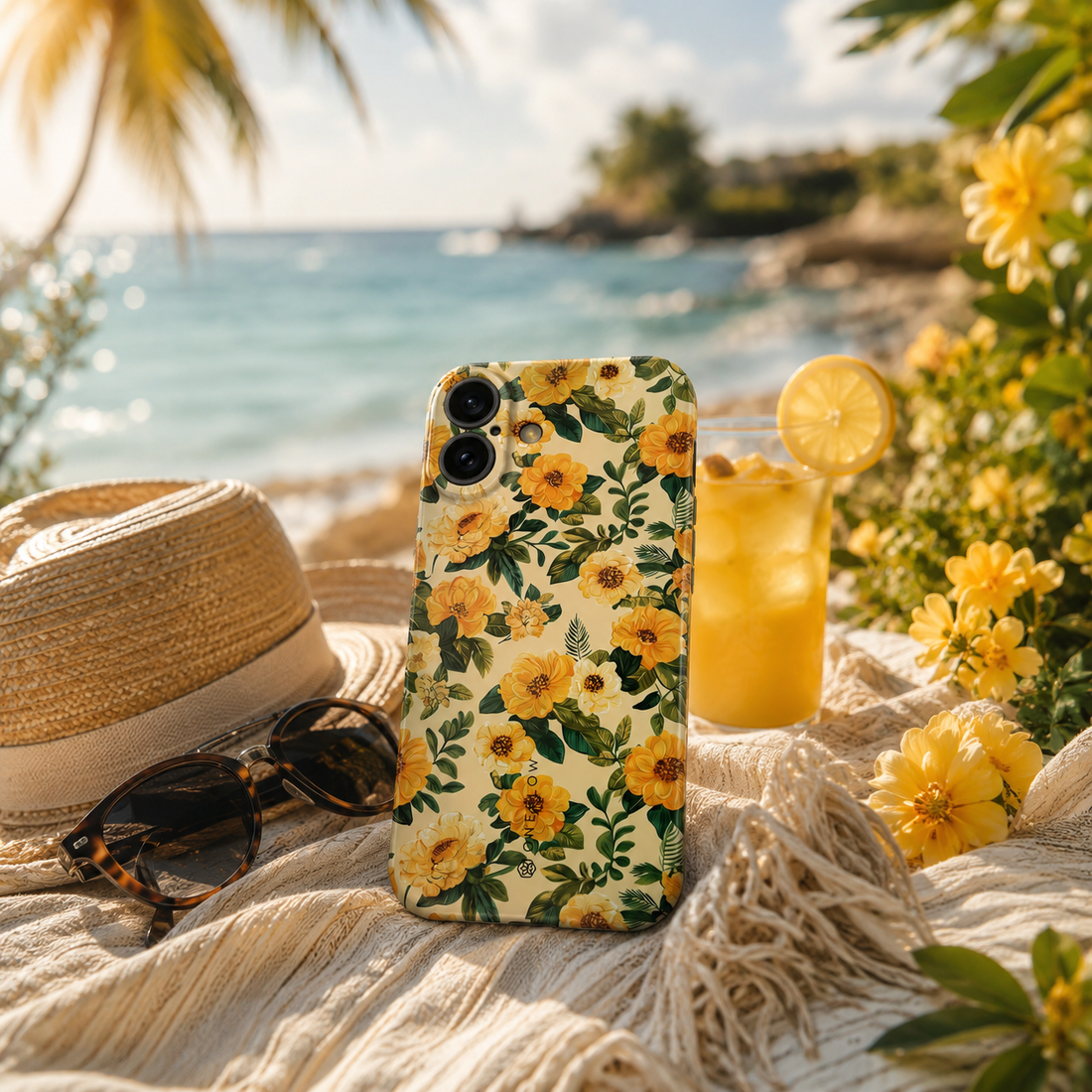 Smartphone-Hülle mit gelbem Blumenmuster am Strand neben Sonnenhut und Sonnenbrille.